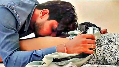 Bearded Indian man passionately kissing woman's neck while gripping her waist in steamy bed scene
