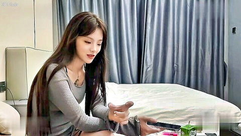 Asian beauty with long dark hair in gray sweater, teasing gesture on bed