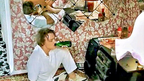 Blond man in white suit drinks beer by stereo as naked woman with bare ass and tits lounges in mirror reflections