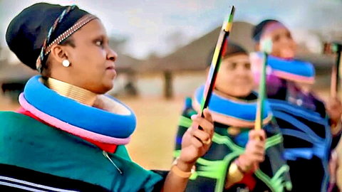Sexy ebony Zulu women in colorful beaded collars and wraps dancing with feathered staffs outdoors