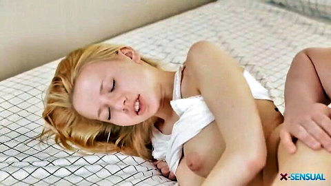 Slim blonde woman topless on bed, hand caressing her thigh in passionate moment