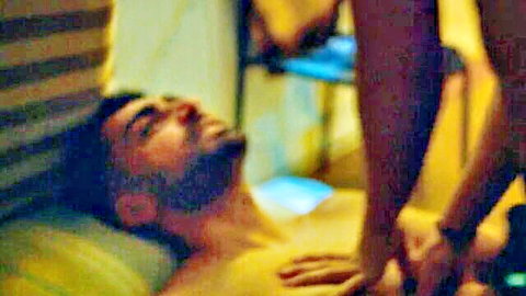 Bearded shirtless hunk lies back eyes closed as woman's thigh straddles and hands grip his hard cock