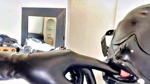 Close-up of latex hood with mouth gag and gloved finger tease in BDSM blowjob