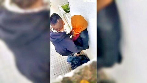 Arab woman in orange hijab bent over by man outdoors