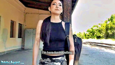 Rae Lil Black as traveler in black tank top and camo pants at train station