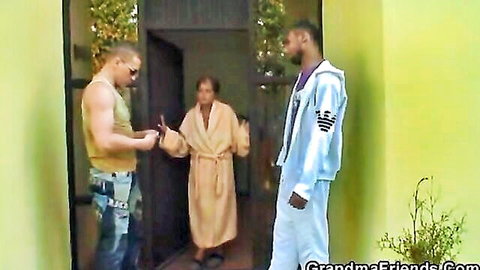 Mature granny in bathrobe greets two muscular young studs at door