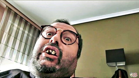 Bearded man with thick glasses making wide-eyed funny open-mouth face in hotel room selfie