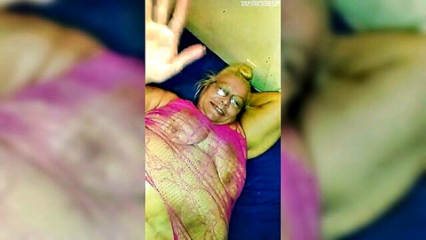 Mature BBW MILF smiles lying back on bed with huge tits and hard nipples visible through sheer pink lace top