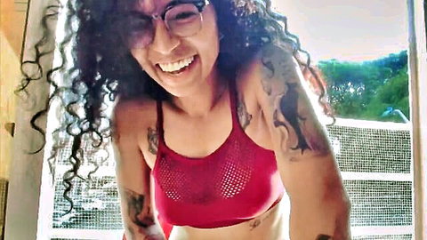 Smiling curly-haired woman in see-through red mesh top on balcony