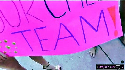 Cheerleader babe holding pink 'OUR TEAM CHEER' sign outdoors flashing sexy bare feet in strappy sandals