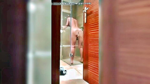 Naked woman bends over in steamy shower exposing wet ass and pink pussy from voyeur angle