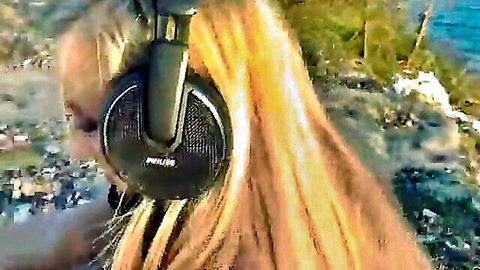 Marry Queen blonde with headphones in outdoor rocky beach setting