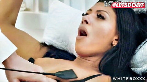 Bound brunette babe moans with open mouth as man holds black paddle to her face in rough BDSM