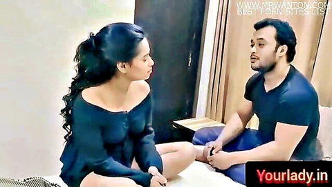 Indian housewife in off-shoulder blue top sits intimately with man on bed showing cleavage