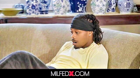 Dreadlocked black stud in yellow tee and sweatpants lounges surprised on couch