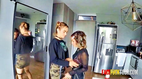 Two goth teens in black outfits touching intimately in kitchen