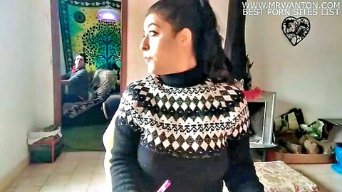 Sexy brunette in patterned sweater holds pen teasingly with man watching from room