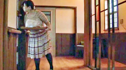 Busty Asian MILF in skirt and stockings leaning over counter, teasing mommy pose