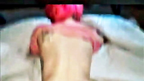 Pink-haired woman nude from behind on bed, bare back exposed