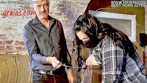 Bound woman fixed to whipping post in BDSM scene with dominant man holding leash