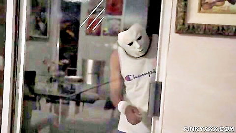 Masked man in white Champions tank top holding towel enters dark room doorway