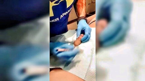 Gloved hand inserts thin metal rod into erect cock urethra on white towel