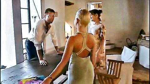 Blonde in backless dress leans over table with shirtless man and brunette in teasing vintage scene