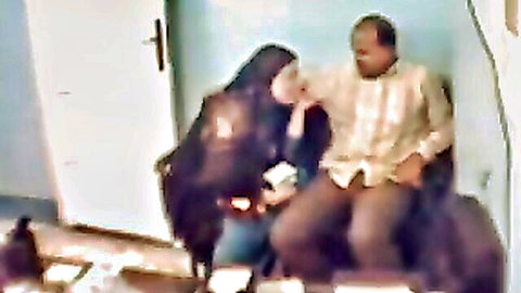 Hijabi Arab woman passionately kissing seated man's face in steamy interracial embrace