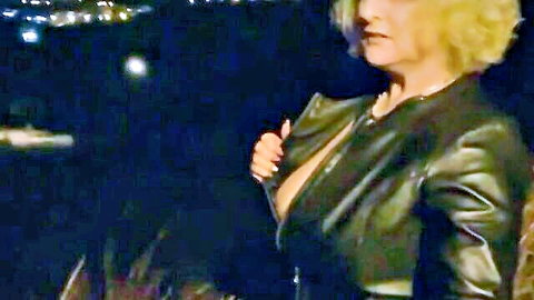 Blonde mature woman in open leather jacket showing deep cleavage at night