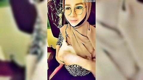 Hijab-wearing Asian woman smiling in glasses, teasing bust in casual top