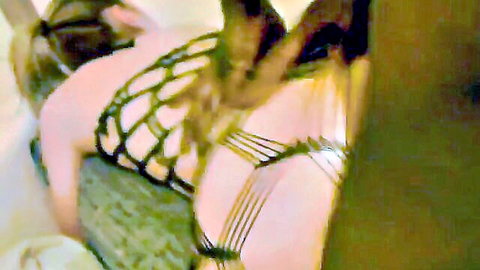 Blonde in sheer fishnet harness exposing pale tits and curves on green couch