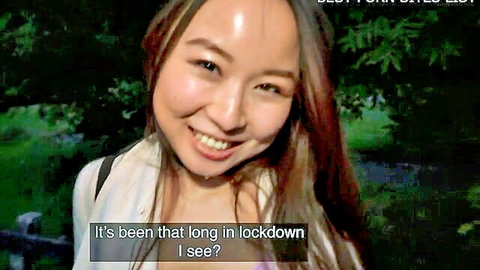 Smiling Asian woman in white top outdoors for cheeky public encounter