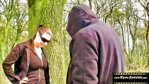 Brunette in sunglasses and blazer meets hooded stranger in woods for outdoor tease