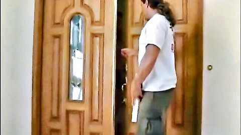 Long-haired brunette man in white t-shirt and cargo pants opening ornate wooden door