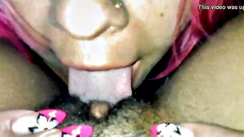 Pink-haired woman with tongue out licks wet pussy close-up in lesbian oral tutorial