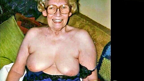 Smiling elderly granny exposes her huge sagging tits topless on couch