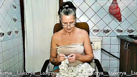 Mature Lukerya knitting topless in openwork white dress, solo