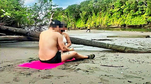 Amateur couple on beach blanket, man in shorts hugs topless woman