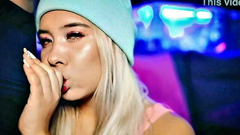 Blonde babe in cyan beanie seductively exhales cigarette smoke with plump red lips pursed like blowjob tease