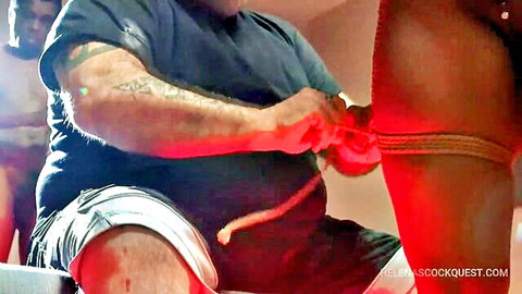 Tattooed man ties red bondage ropes around pale skinny woman's exposed thigh and ass