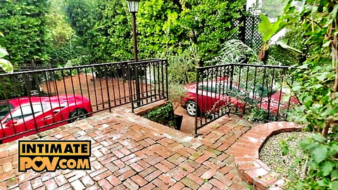 POV outdoor brick patio with lush greenery black railing and sleek red Ferrari sports car