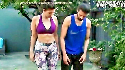 Indian yoga teacher in purple sports bra and leggings with fit guy outdoors