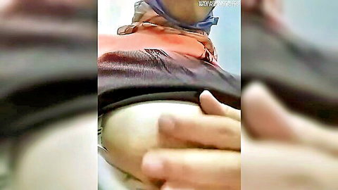 Blurry amateur video thumbnail of woman in orange top and black skirt touching her curves