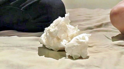 Crumpled white tissue on beige bed sheets beside dark pants and bare thigh after sex