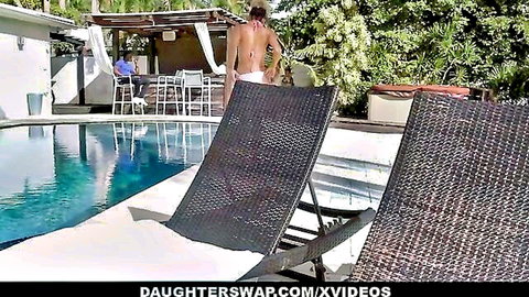 Topless brunette in white thong bikini bends over poolside loungers outdoors