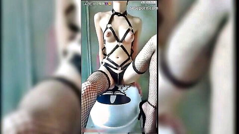 Asian beauty in black harness lingerie and fishnets spreads legs exposing shaved pussy