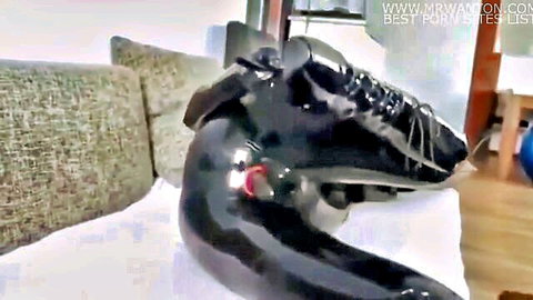 Solo woman in shiny black latex catsuit bent over on couch, fetish tease