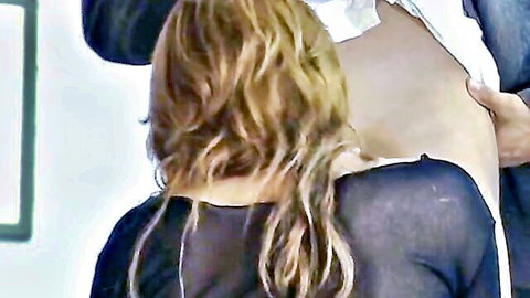 Blonde woman undressed from behind by man in sheer top, office tease
