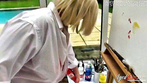 Mature blonde artist Lacey Starr in white shirt bending over canvas seductively