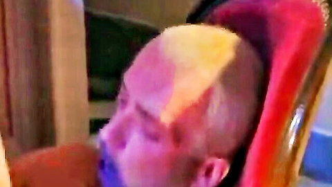 Blurry closeup of bald man with flushed face leaning back in red chair